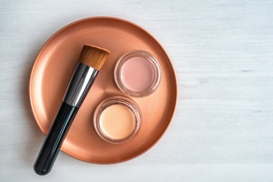 Make-up foundation brush beauty products cream blush and contour pots on mixing palette for makeup artist. Top view on white wooden background.