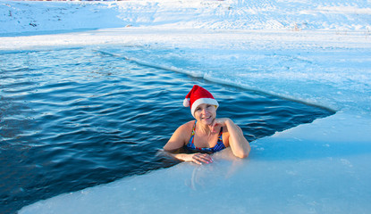 woman in a lake in winter in a swimsuit in a santa hat, winter extreme swimming quenching