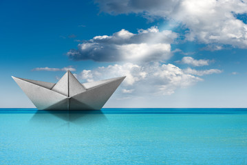 Obraz premium Paper boat in the turquoise sea with blue sky and clouds