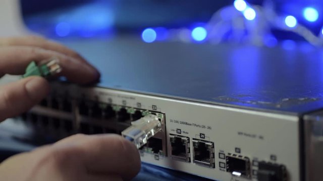 Network engineer securing Ethernet cables into switch with blue lights background