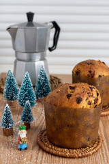 Top view of two panettones with metal coffee maker, small Christmas trees and Wise Man on wooden table with sugar grains