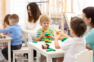 Group of preschool children and teacher playing with building blocks together in kindergarten