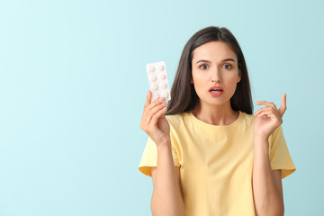 Young woman with pills on color background