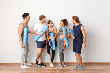 Group of people with yoga mats near light wall