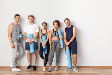 Group of people with yoga mats near light wall