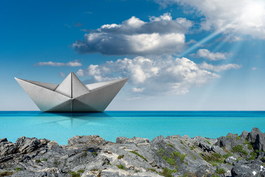 Paper boat in the turquoise sea with blue sky and clouds