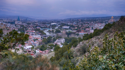 Obraz premium Panorama view city of Tbilisi in cloudy weather from the surrounding mountains in autumn evening during sunset time