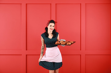 Portrait of tattooed pin-up housewife with buns on color background