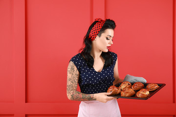 Portrait of tattooed pin-up housewife with buns on color background