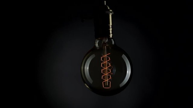Flickering old fashion tungsten Edison light bulb lamp over black background. Slow motion shot
