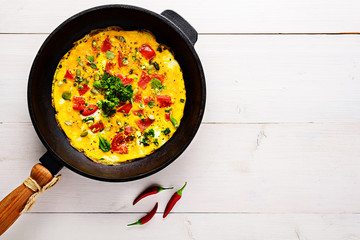 fried eggs with tomatoes and chilli in an old cast iron skillet on a white wooden background with a copy of the space