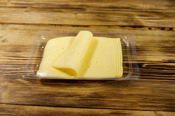 Slices of cheese in disposable plastic packing box on wooden table