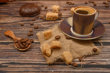 A Cup of coffee, pieces of brown sugar, marshmallows in chocolate and coffee beans on a wooden spoon on a wooden background. Close up.