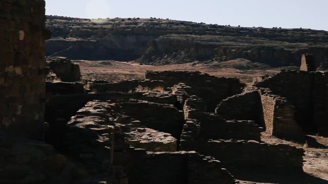 Panning across the shadowy parts of Chetro Ketl when the sun is high in the sky causing flare and casting dark shadows across blocked parts of the landscape. These are Anasazi ruins in Chaco Canyon NM