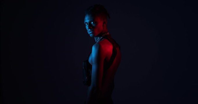Shirtless african man with bag and chain necklace turning around in ultraviolet light