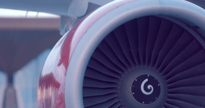 The plane is standing next to the airport building, the red turbine of the plane rotates slowly