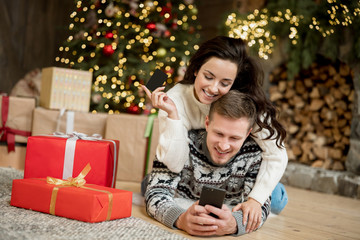 Obraz na płótnie Canvas Young couple beautiful woman and handsome man both wearing warm sweaters sending online greetings in room decorated for celebrating the new year christmas festive mood