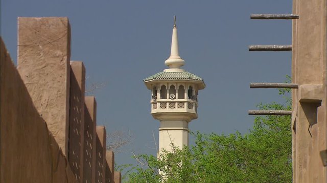 Medium  close-up, low-angle still shot  on a bright sunny day of an ancient Mosque  minaret  with a speaker between two traditional arabic buildings, Bastikiya, Dubai, UAE