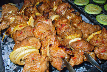 Pork skewers on grill with coals, cooking process. Zucchini slices on background.