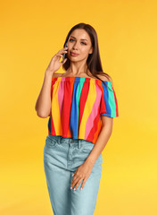 Beautiful young woman talking by phone on yellow background
