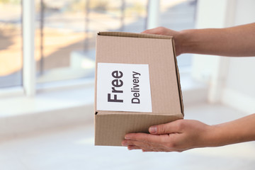 Courier holding parcel with sticker Free Delivery indoors, closeup