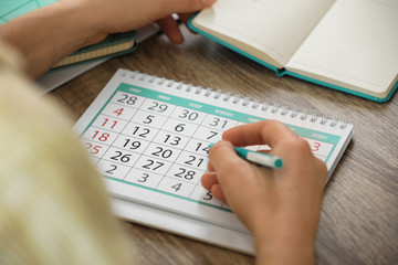 Woman marking date in calendar at wooden table, closeup