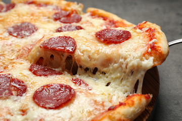 Taking slice of tasty pepperoni pizza on table, closeup