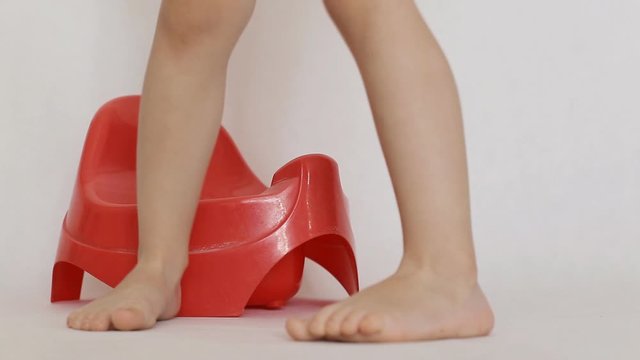 Little girl sits on a red pot. Accustoming to a toilet of children, background, hygiene