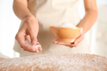 Young woman having body scrubbing procedure with sea salt in spa salon, closeup