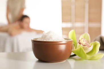 Bowl with sea salt and orchid flower on white table in spa salon