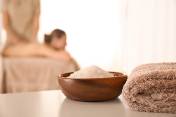 Bowl with sea salt on white table in spa salon