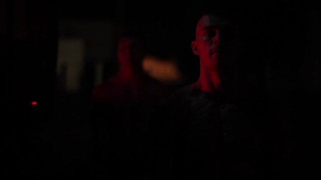 Two muscular firefighters doing biceps exercises in the light of blinking fire truck emergency lights at night. Close view