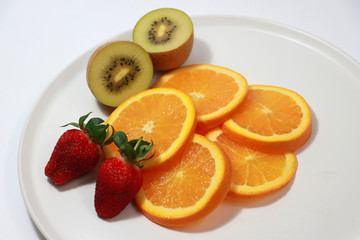 The thin round pieces of orange slices put together with strawberry and kiwi fruit on the white dish.