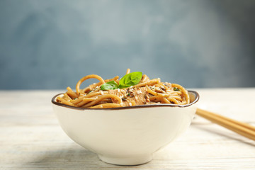 Tasty buckwheat noodles with meat in bowl on white wooden table