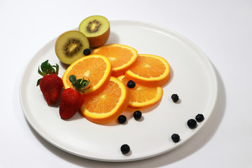 The thin round pieces of orange slices pile together with strawberry, kiwi fruit, blueberry on the white dish.