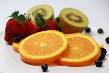The thin round pieces of orange slices with out focus strawberry, kiwi fruit and blueberry on the white dish.