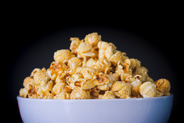 Delicious popcorn with caramel in bowl on black color background