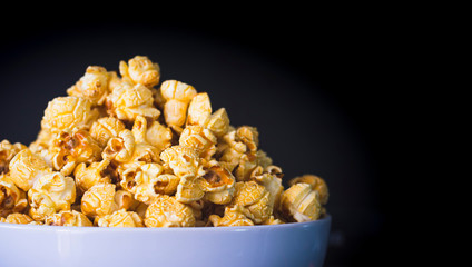 Delicious popcorn with caramel in bowl on black color background