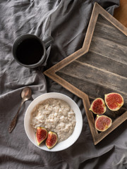 porridge with figs on coconut milk on a gray background and a wooden stand. Ingredients for a healthy breakfast.