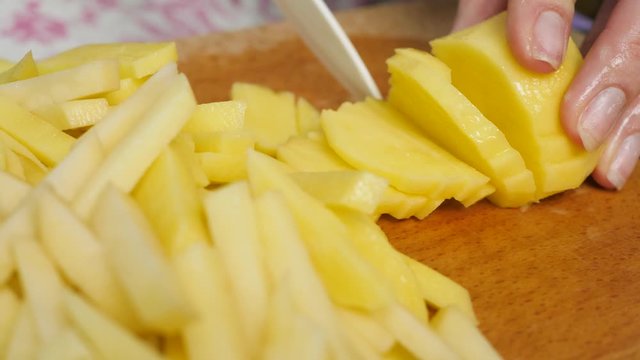 Woman at kitchen cutting thin slices of raw potato by knife. Dishes with vegetables. Concept of cooking and healthy eating