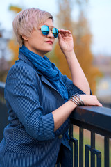 Beautiful elegant blond woman posing in autumn city park, dressed in blue jeans and jacket