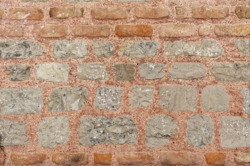 Gray stone wall texture with red fire bricks in the upper part. Pasted with red colored cement.