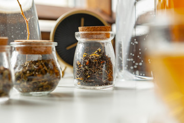 Glass jars with dry tea leaves close up on white table