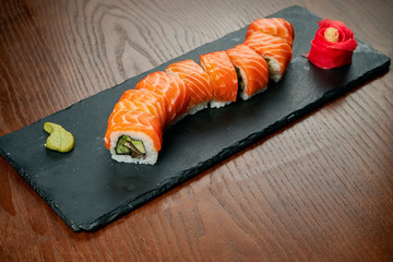 Sushi rolls with cucumber and salmon on a black slate board on a wooden background. Japanese cuisine. Close up