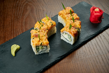Sushi rolls with cucumber, philadelphia cheese and eel on a black slate board on a wooden background. Japanese cuisine. Close up