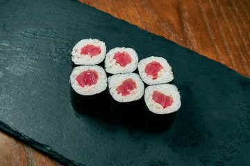 Sushi maki rolls with tuna on a black slate board on a wooden background. Japanese cuisine. Close up