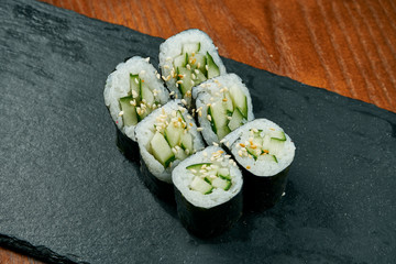 Sushi maki rolls with cucumber on a black slate board on a wooden background. Japanese cuisine. Close up
