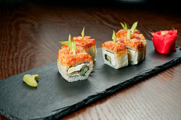 Sushi rolls with cucumber, philadelphia cheese, caviar and salmon on a black slate board on a wooden background. Japanese cuisine. Close up
