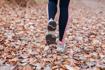 Close-up of feet of a runner running in autumn leaves in park