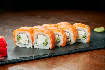Sushi rolls with cucumber, philadelphia cheese and salmon on a black slate board on a wooden background. Japanese cuisine. Close up